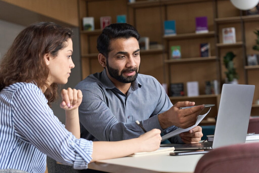 A career coach reviews documents with a young student at a desk, with a laptop open in front of them during a one-on-one mentoring session.